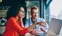 Female graphic designer pointing with finger on laptop computer during collaboration with caucasian colleague