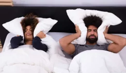 Elevated View Of Young Couple Lying In Bed Covering Their Ears With Pillow Elevated View Of Young Couple Lying In Bed Covering Their Ears With Pillow