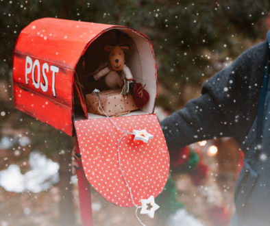 woman holds a red polka dot retro mailbox with Christmas gifts toys as well as a congratulatory letter from Santa on a background of fir trees.