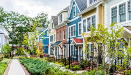 Row of colorful, red, yellow, blue, white, green painted residential townhouses, homes, houses with brick patio gardens in summer