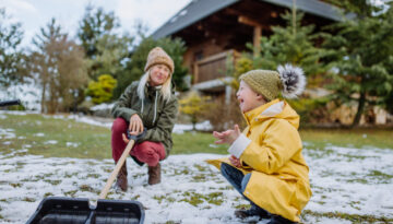 Boy with Down syndrome with his mother clearing snow from path with shovel in front of house.