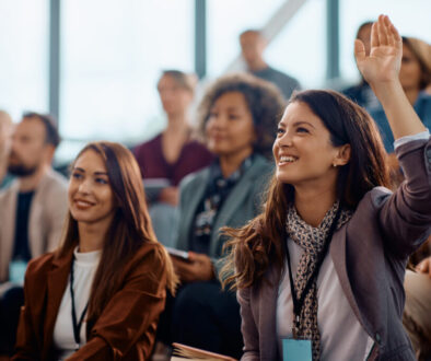 Happy entrepreneur raising her hand to answer a question during business conference in convention center.