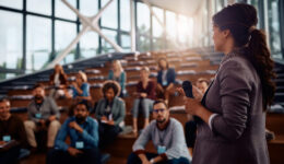 Female business leader talking to group of seminar attendees at convention center.