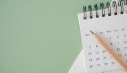 top view of white calendar and sharpen brown pencil on green background, schedule, timeline, planning concept