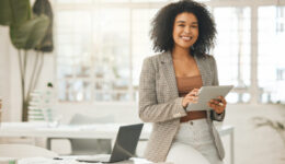 Happy businesswoman using a digital tablet. Young leading businesswoman using a wireless tablet. Creative designer working in her agency. Designer standing in her office using an online app