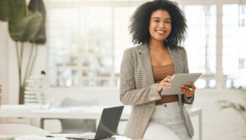 Happy businesswoman using a digital tablet. Young leading businesswoman using a wireless tablet. Creative designer working in her agency. Designer standing in her office using an online app