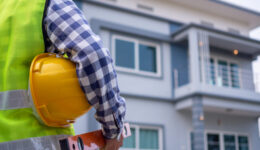 The male inspector was watching the supervised house, carrying equipment and a helmet, wearing a vest in the development of housing and real estate concepts.