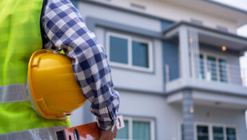 The male inspector was watching the supervised house, carrying equipment and a helmet, wearing a vest in the development of housing and real estate concepts.