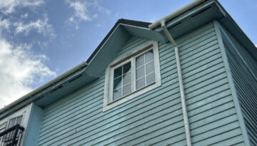 Blue Wooden House Exterior With Window and Gutter Against Bright Sky
