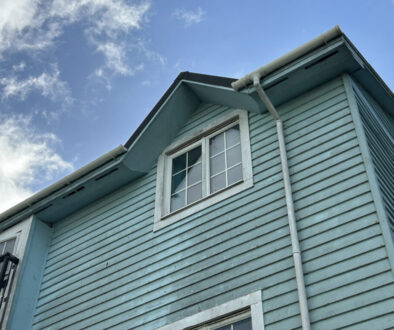Blue Wooden House Exterior With Window and Gutter Against Bright Sky